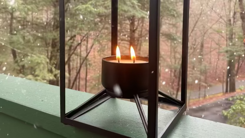 Black metal lantern with a candle on a green surface, forest background